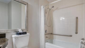 Un baño con inodoro, lavamanos, espejo, ducha con barra de apoyo y bañera.