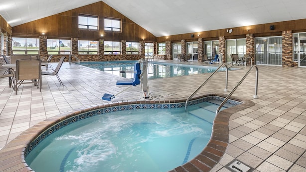 Una piscina interior con un jacuzzi, sillas de descanso y vistas al exterior.