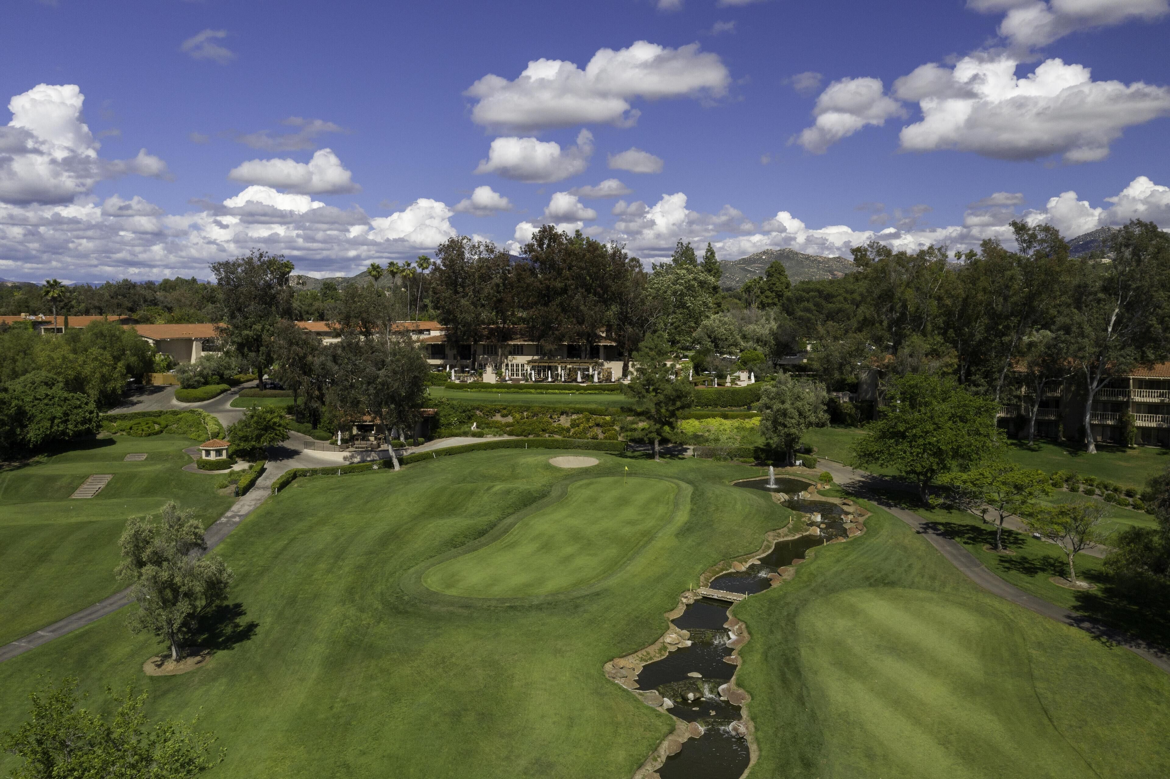 Un campo de golf con un estanque, árboles y un club de campo al fondo.