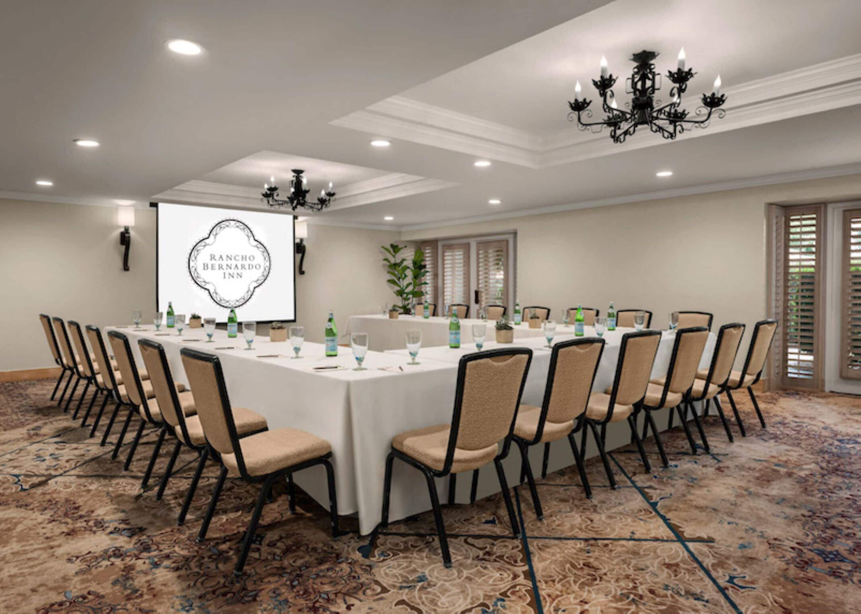 Une salle de conférence équipée d’une longue table, de chaises et d’un écran de projection affichant le nom de l’hôtel.