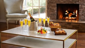 A dining table with champagne, fruit, and pastries, a fireplace, and a cozy chair in a room with a stone wall. - Rancho Bernardo Inn (San Diego)