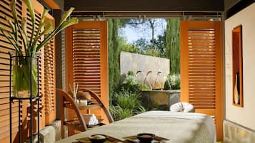 Relax in this serene spa room with a large bed, a wooden chair, and a soothing view of a water feature.