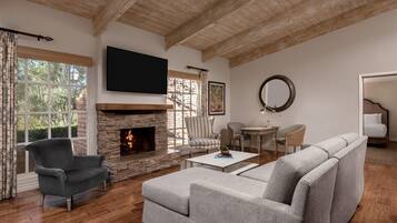 A living room with a stone fireplace, a flat-screen TV mounted above it, a grey sofa, a striped armchair, and a round mirror on the wall.