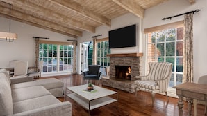 A spacious living room with a stone fireplace, large windows, and a flat-screen TV mounted on the wall. - Rancho Bernardo Inn (San Diego)
