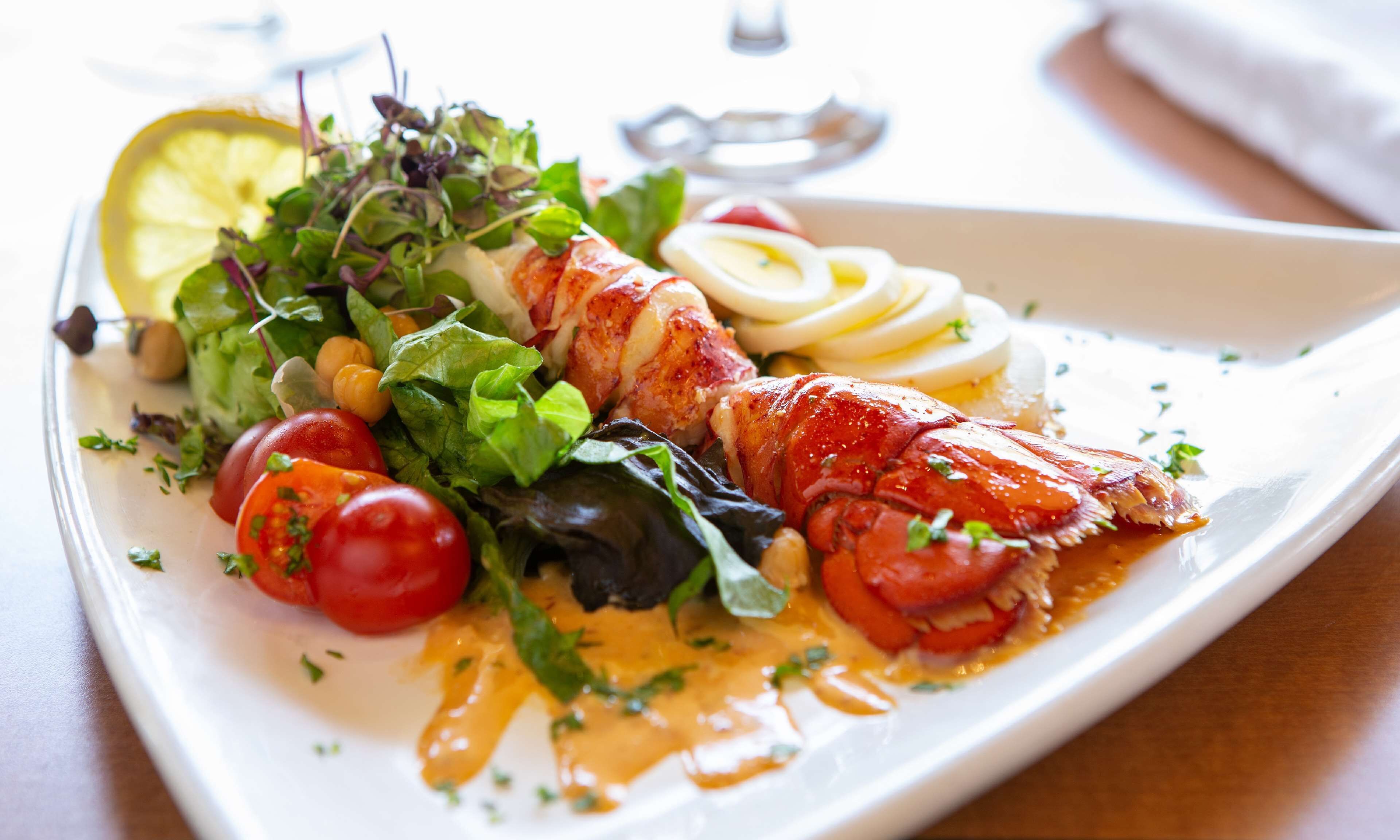 En tallerken mad med hummerhale, salat, cherrytomater og citronskiver.