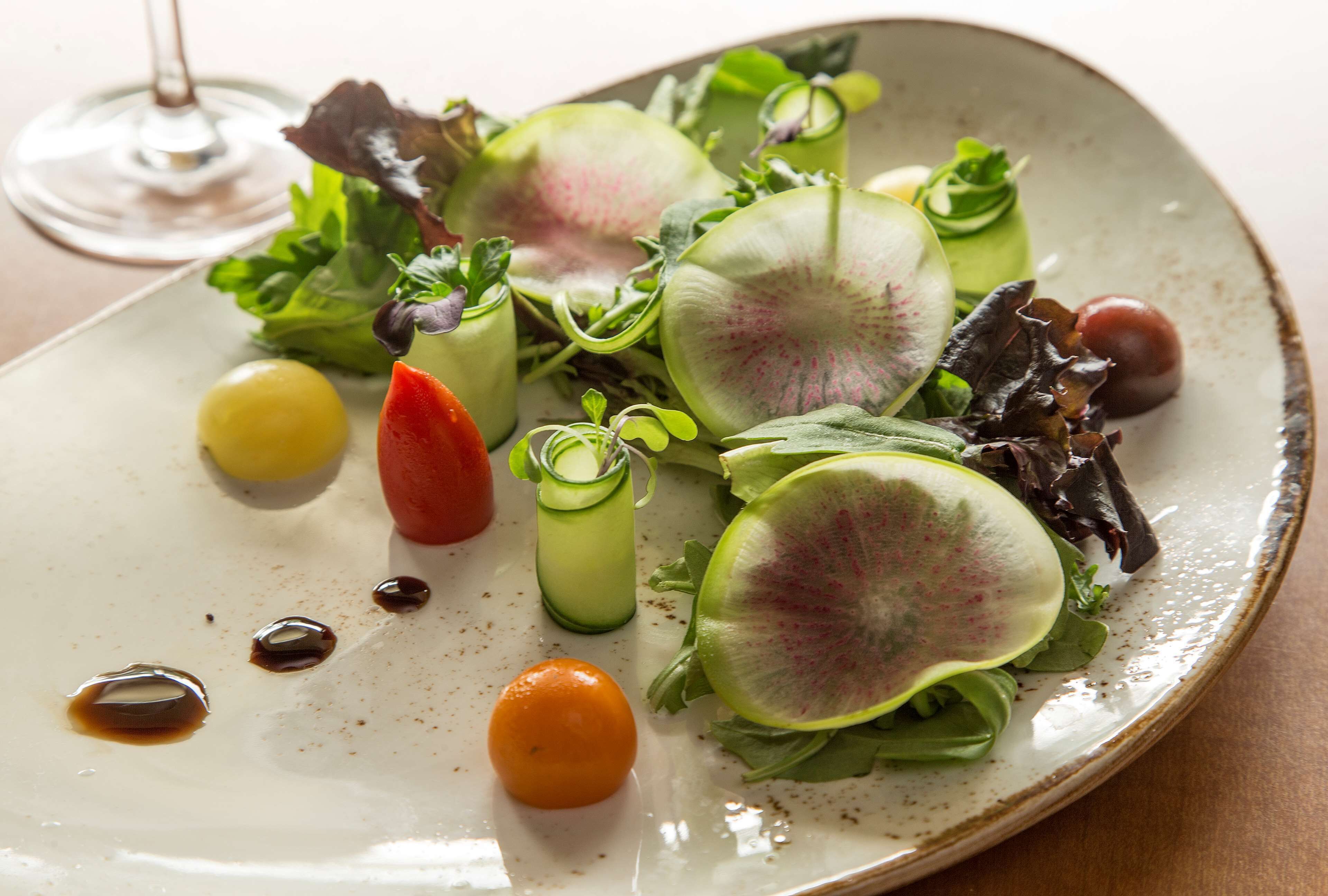 A plate with a salad, a glass of wine, and a small orange.