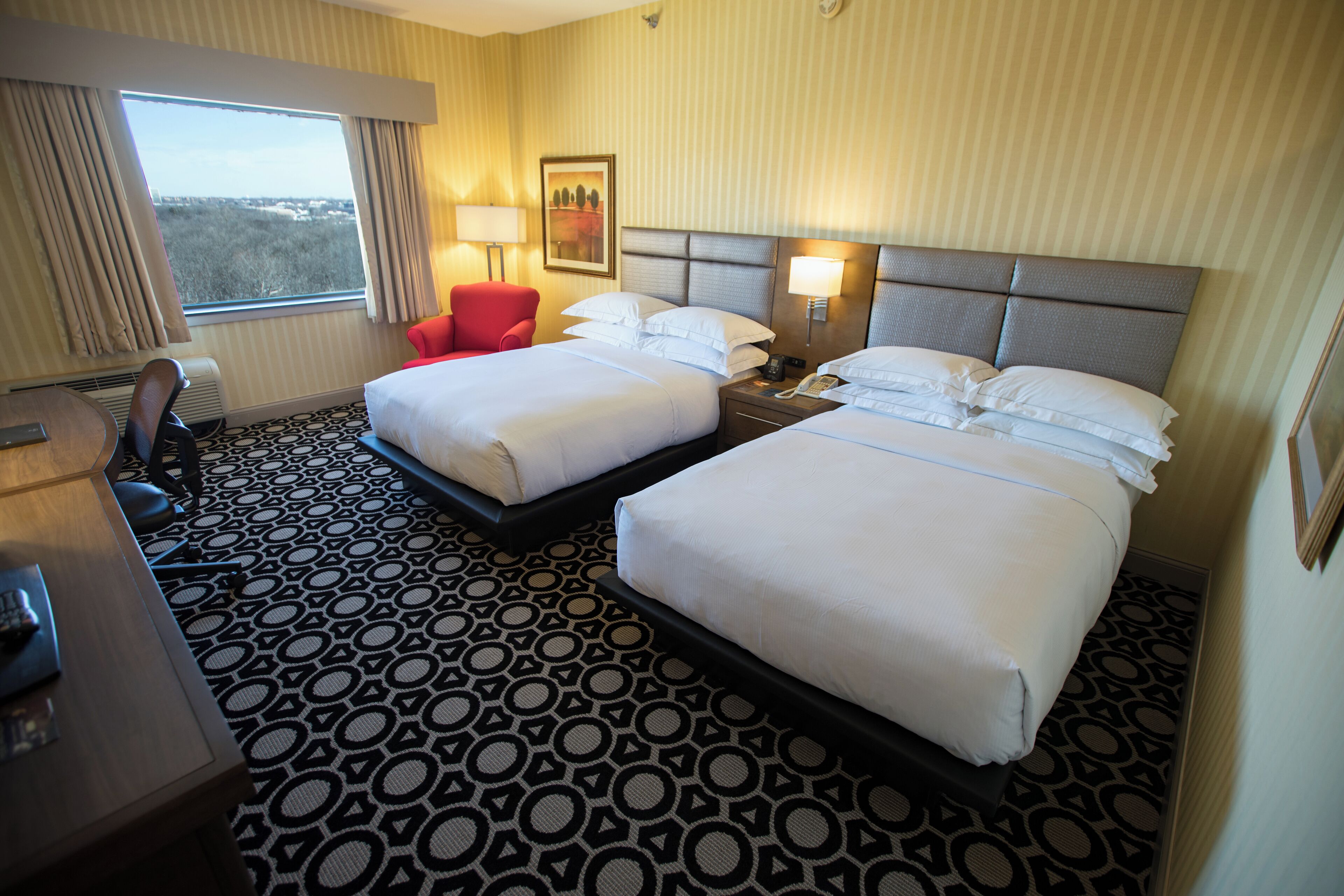 A hotel room with two beds, a desk, a chair, and a window with curtains.