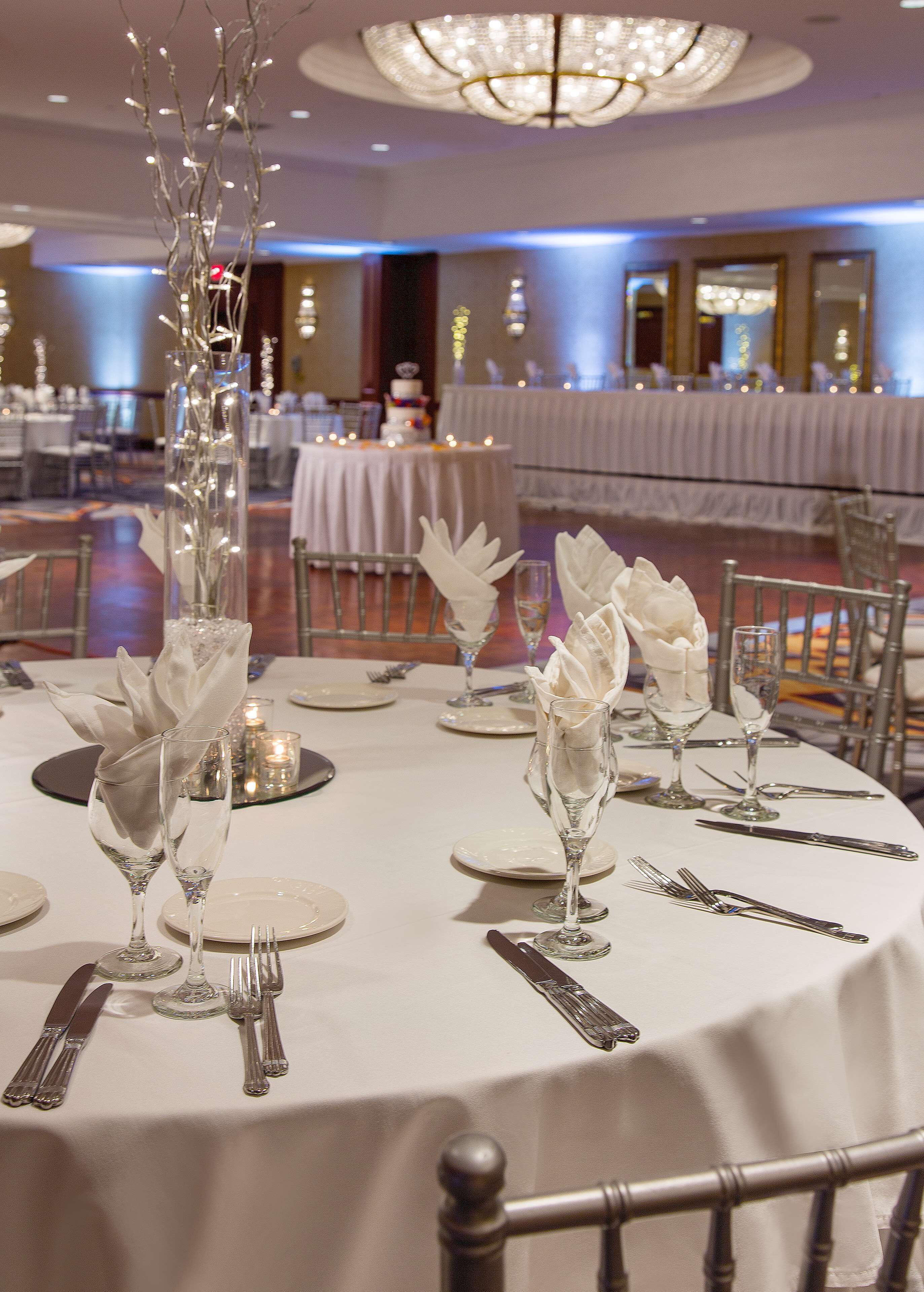 Une salle de banquet avec des tables rondes dressées pour un événement formel, agrémentée de verres en cristal, de serviettes blanches et de décorations de table élégantes.