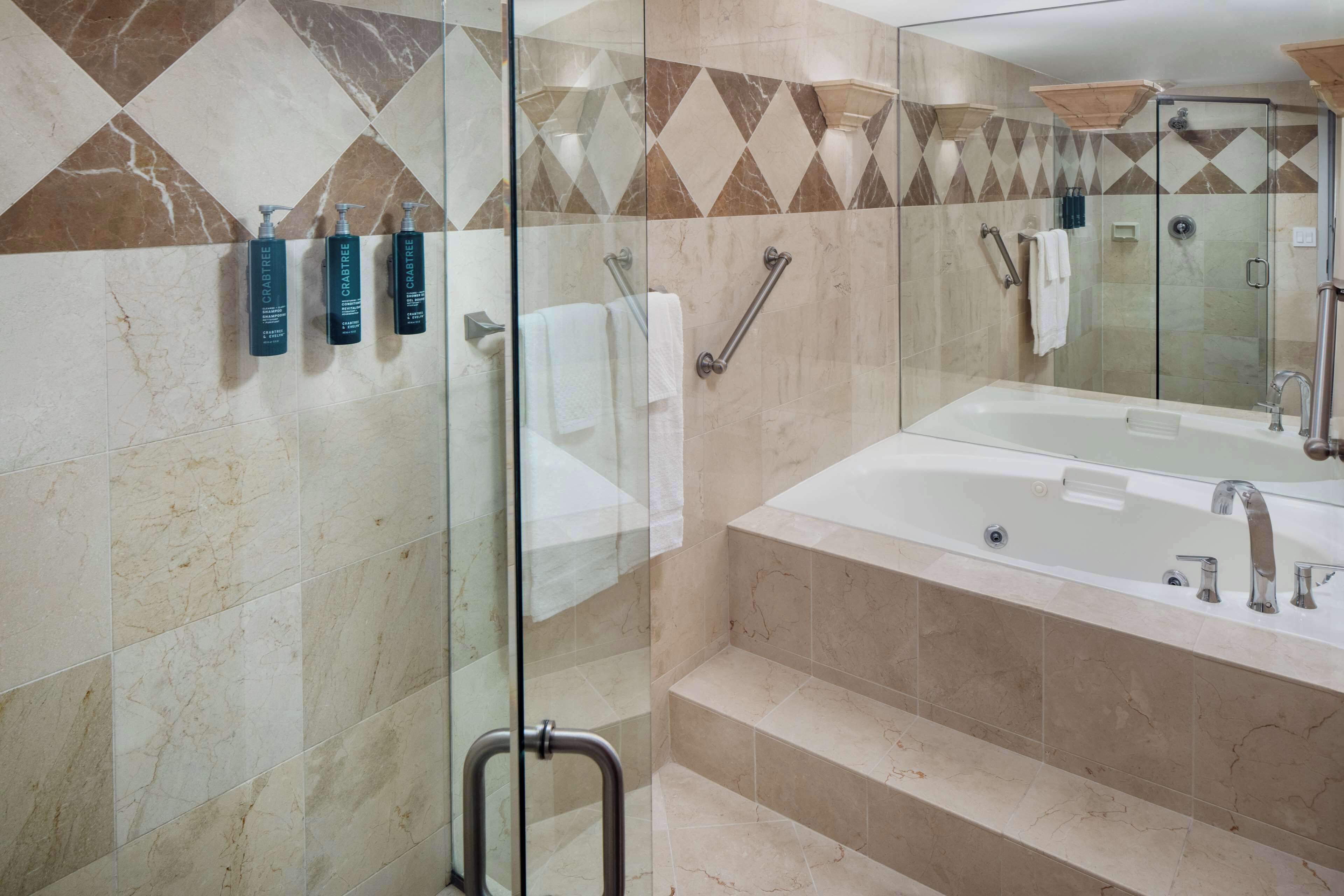 A modern bathroom with a glass-enclosed shower, a large bathtub, and marble tiles.