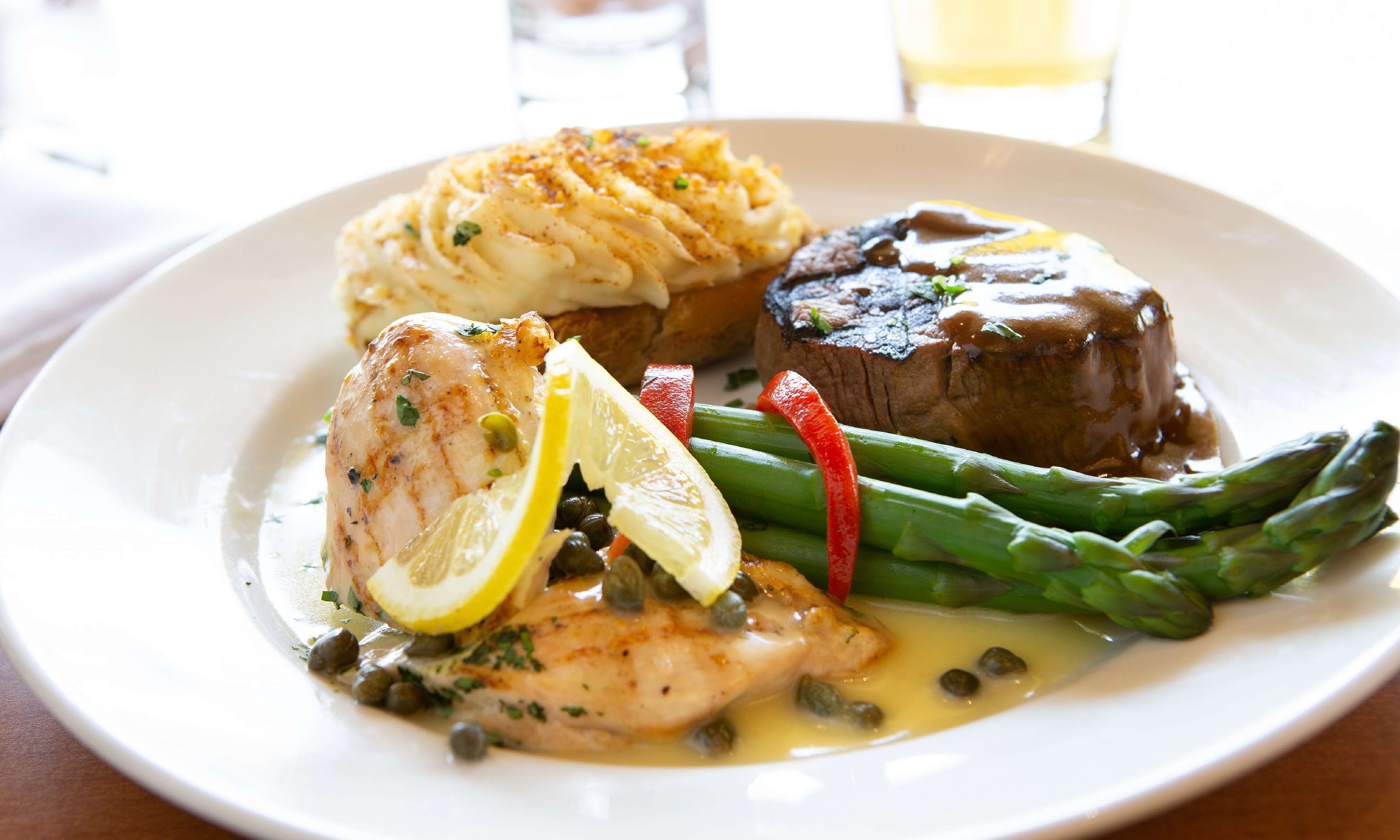Une assiette contenant un morceau de poulet, des asperges, une tranche de citron et un steak nappé de sauce.