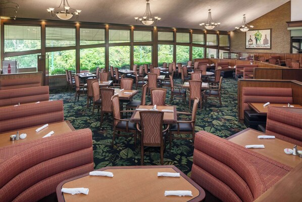 A restaurant with booths and tables, large windows with a view of greenery, and a chandelier.