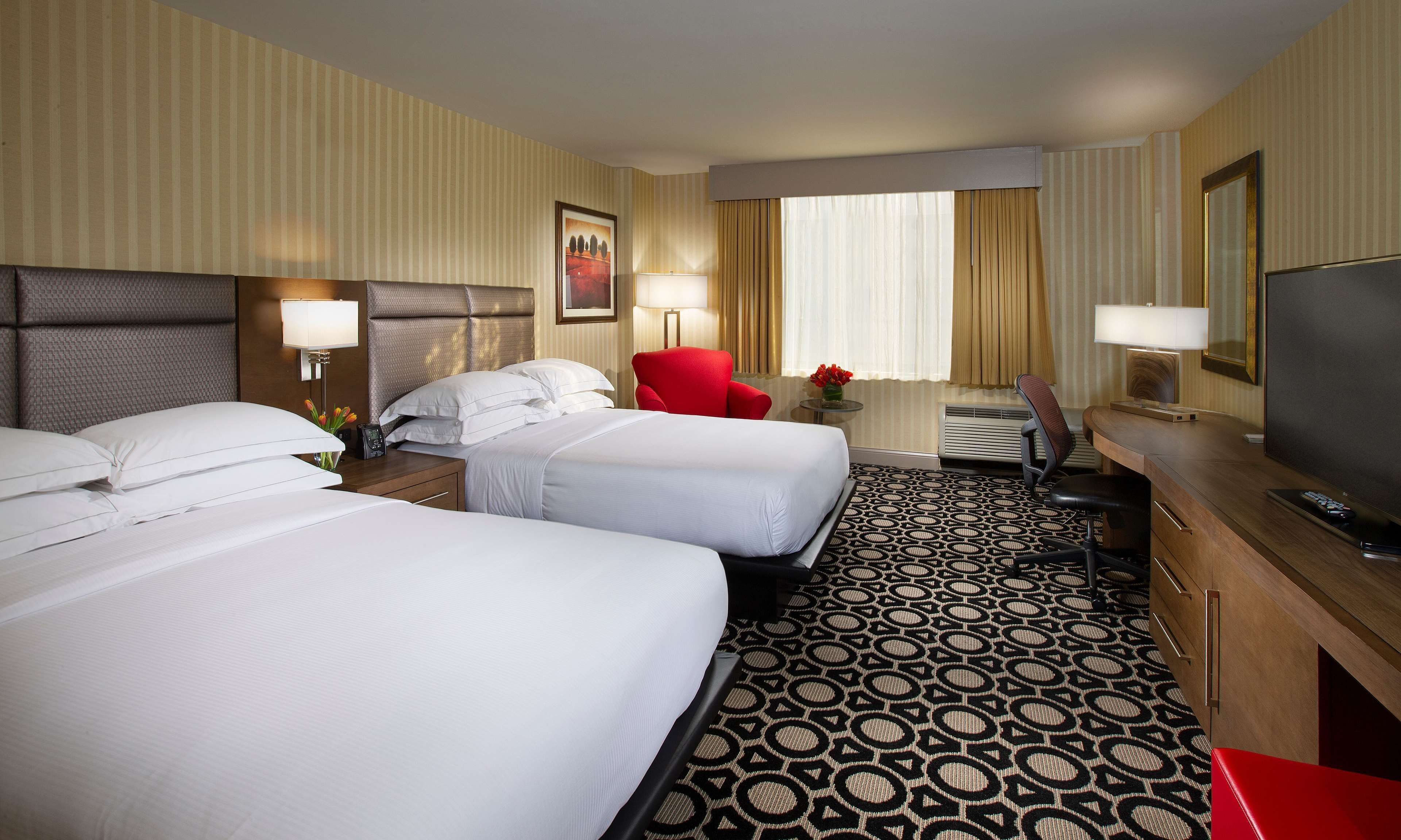 A hotel room with two beds, a desk, a TV, and a red chair.