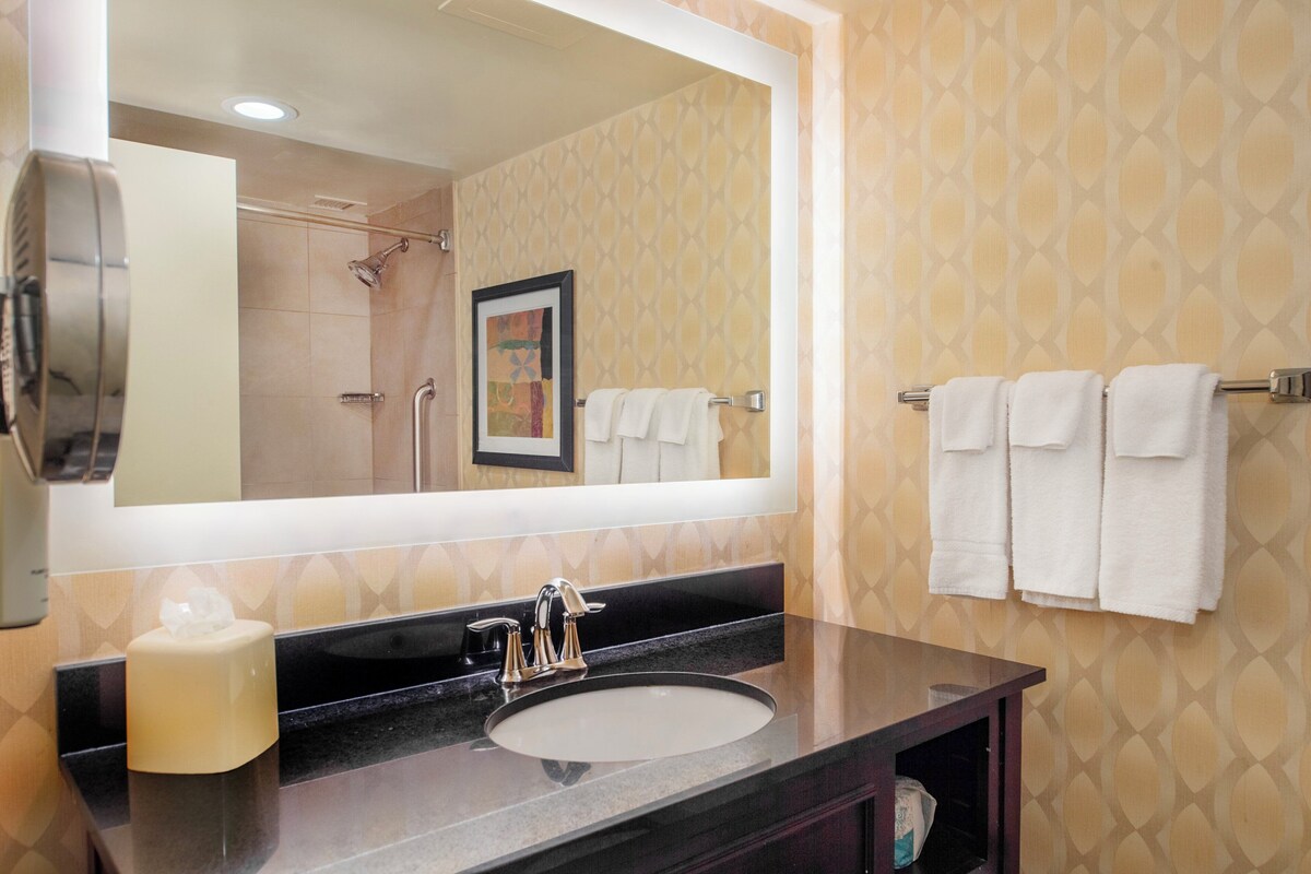 A bathroom with a large mirror, a sink, and a towel rack with towels.