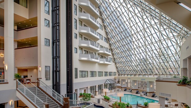 A multi-level hotel interior with a large glass atrium, a swimming pool, and multiple balconies.