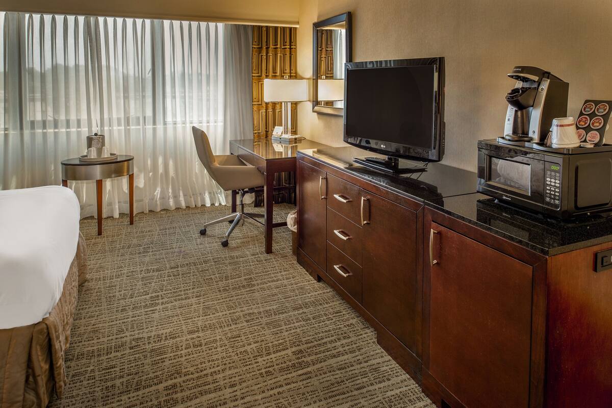 Une chambre d’hôtel équipée d’un lit, d’un bureau avec une chaise, d’une télévision, d’une machine à café et d’un four à micro-ondes.