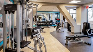 A gym with cardio machines, weightlifting equipment, and dumbbells.