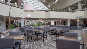 A spacious indoor area with multiple seating arrangements, including tables and booths, and a high ceiling with a geometric glass structure.