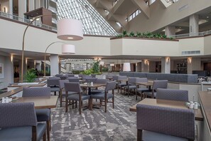 Een ruime binnenruimte met diverse zithoeken, waaronder tafels en zitjes, en een hoge plafond met een geometrisch glazen constructie.