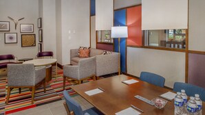 A hotel room with a conference table, two armchairs, a sofa, and a patterned rug.