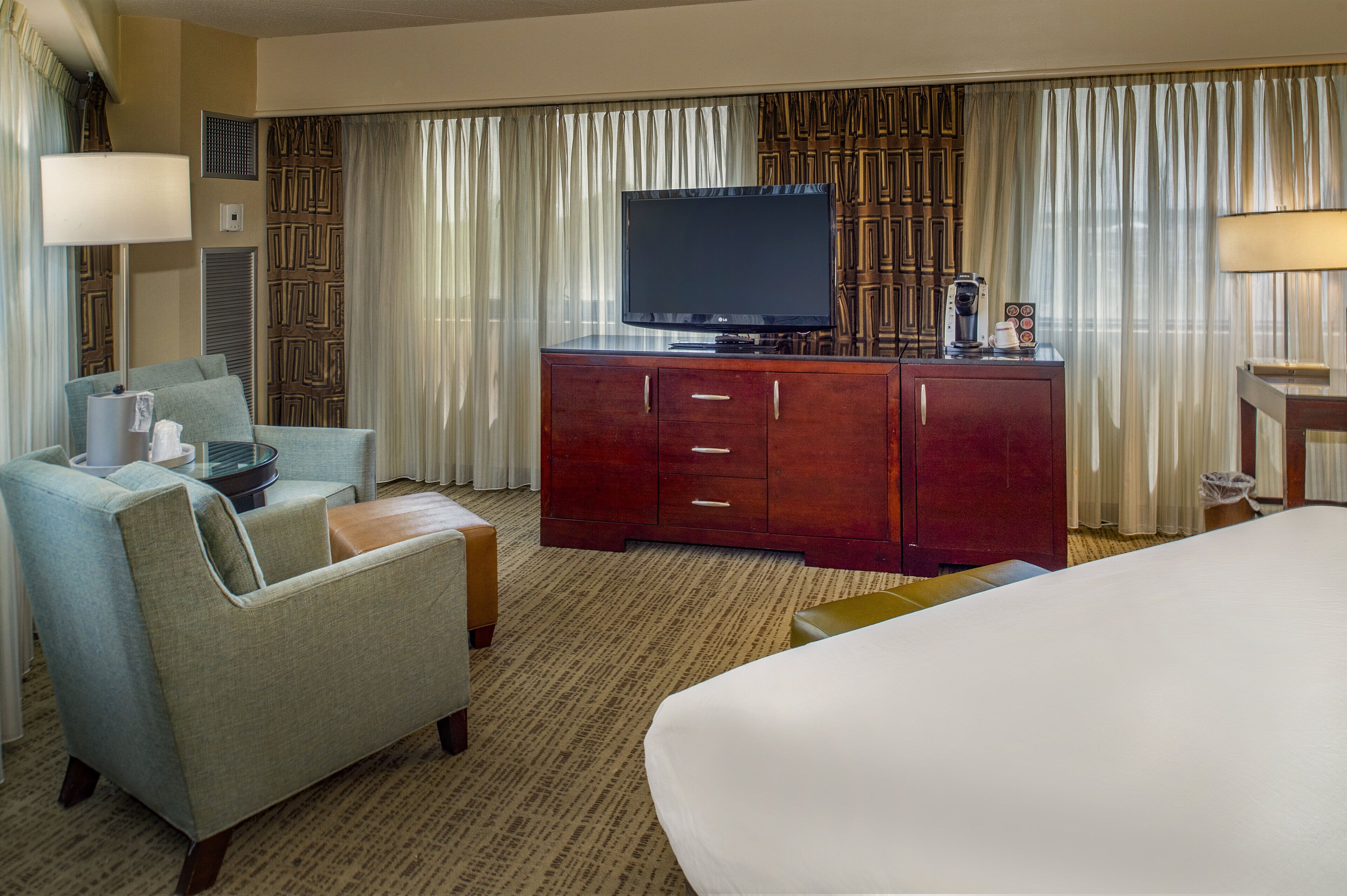 A hotel room with a bed, a television on a wooden cabinet, a sofa, and a coffee maker.