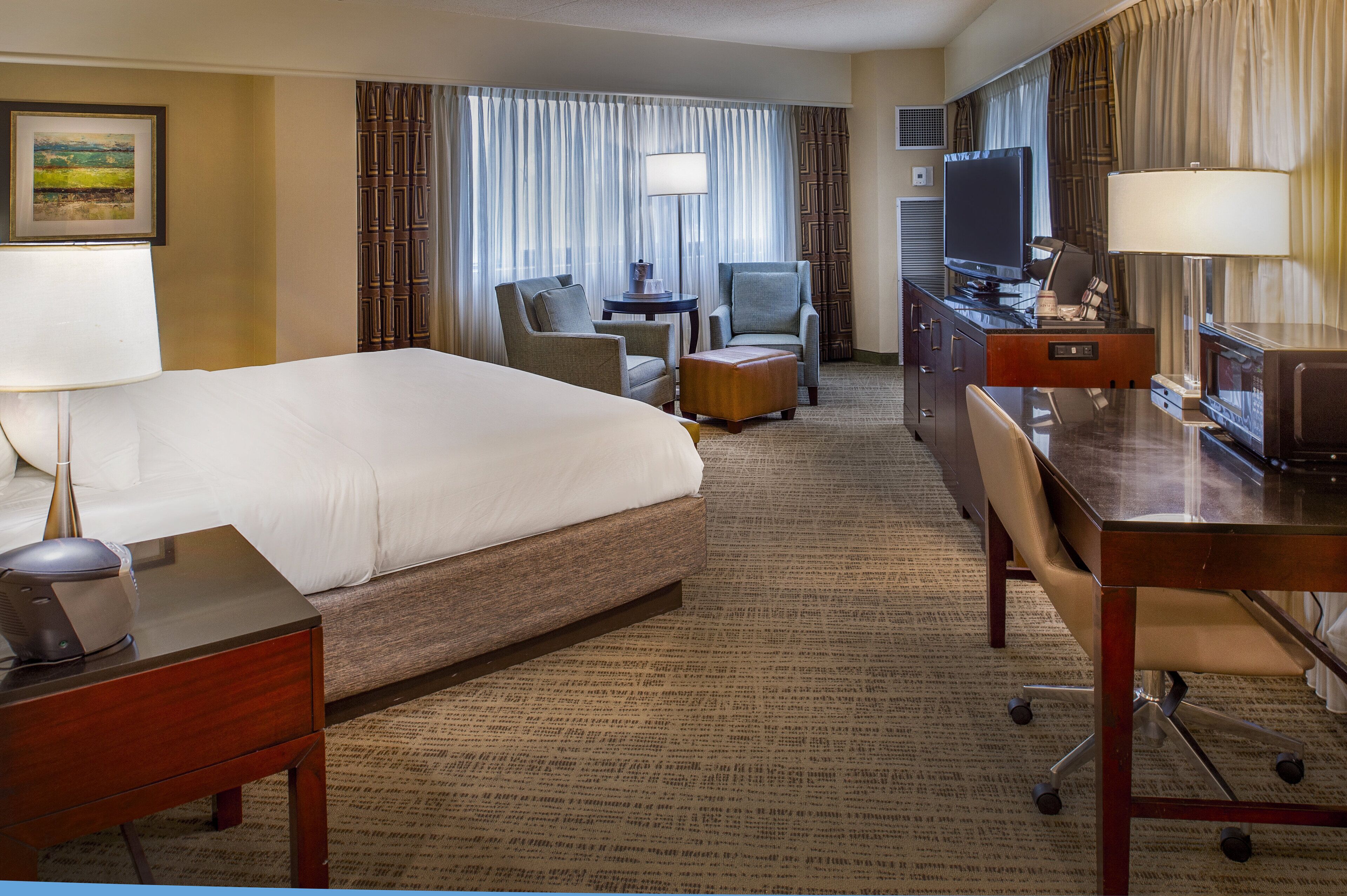 Une chambre d’hôtel avec un grand lit, un bureau avec un ordinateur, une chaise, une petite table et un téléviseur.