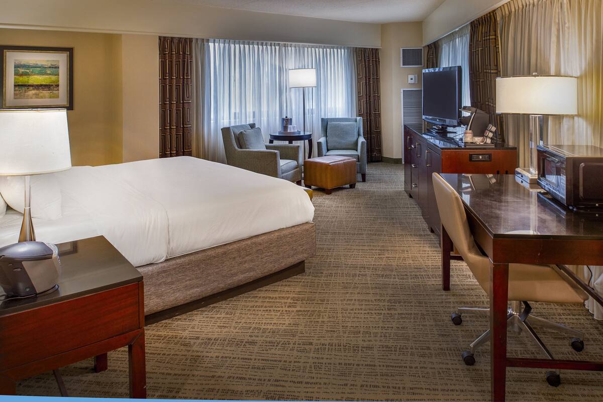 Une chambre d’hôtel avec un grand lit, un bureau avec un ordinateur, une chaise, une petite table et un téléviseur.