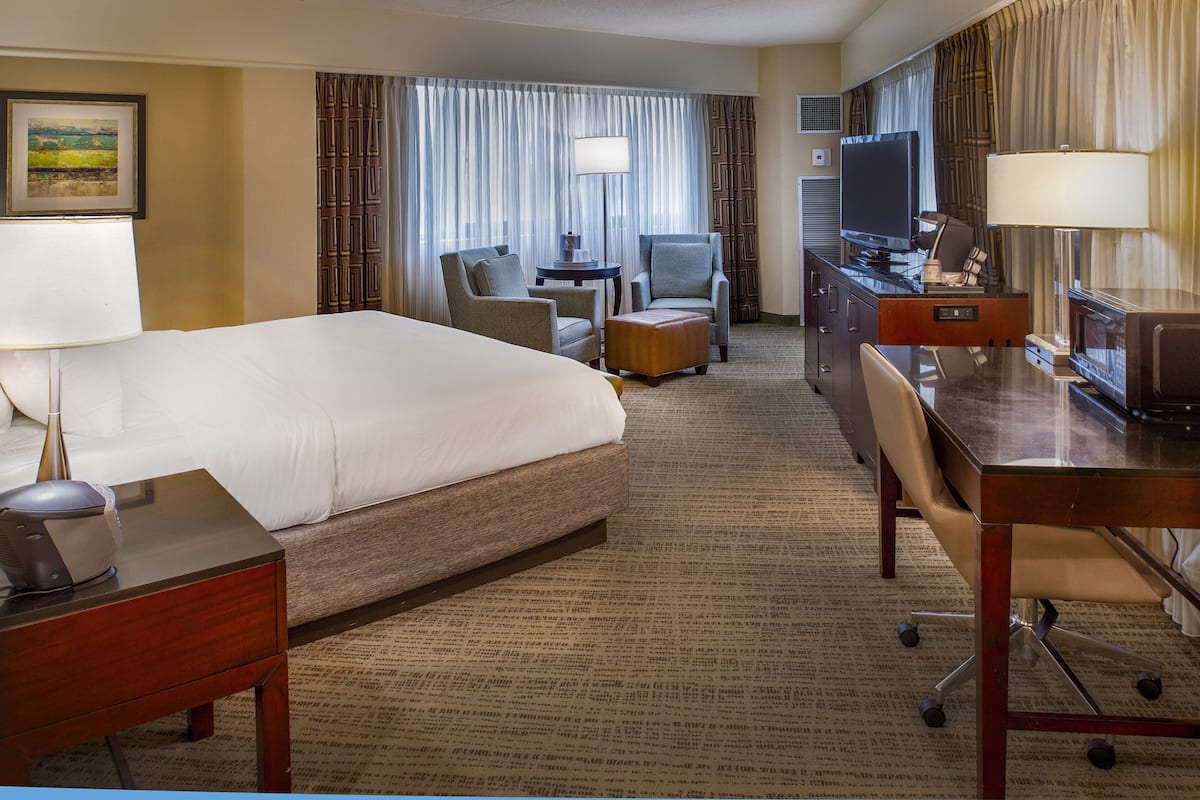 Une chambre d’hôtel avec un grand lit, un bureau avec un ordinateur, une chaise, une petite table et un téléviseur.
