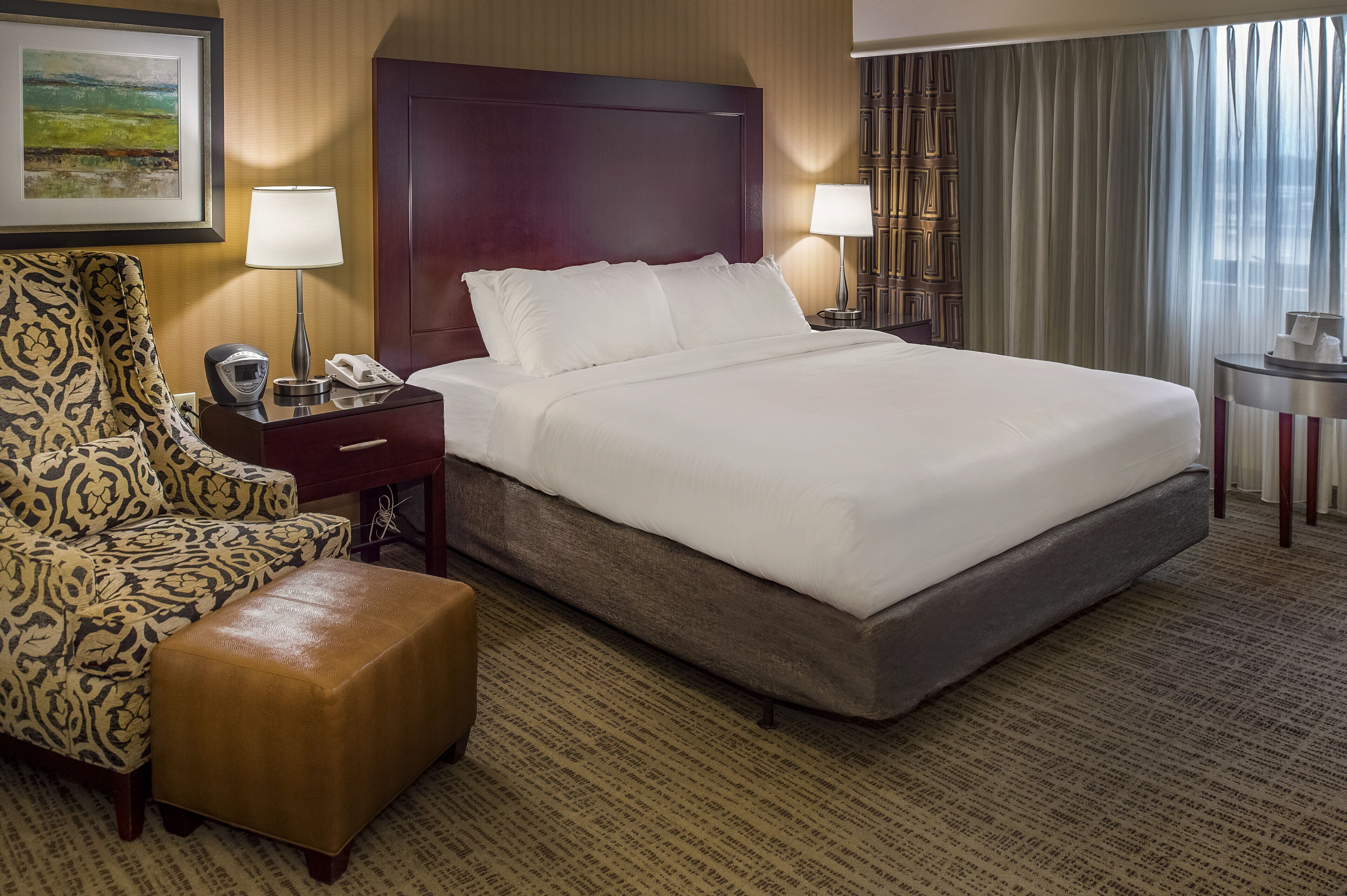 A hotel room with a large bed, a chair, a desk with a lamp, and a small table.