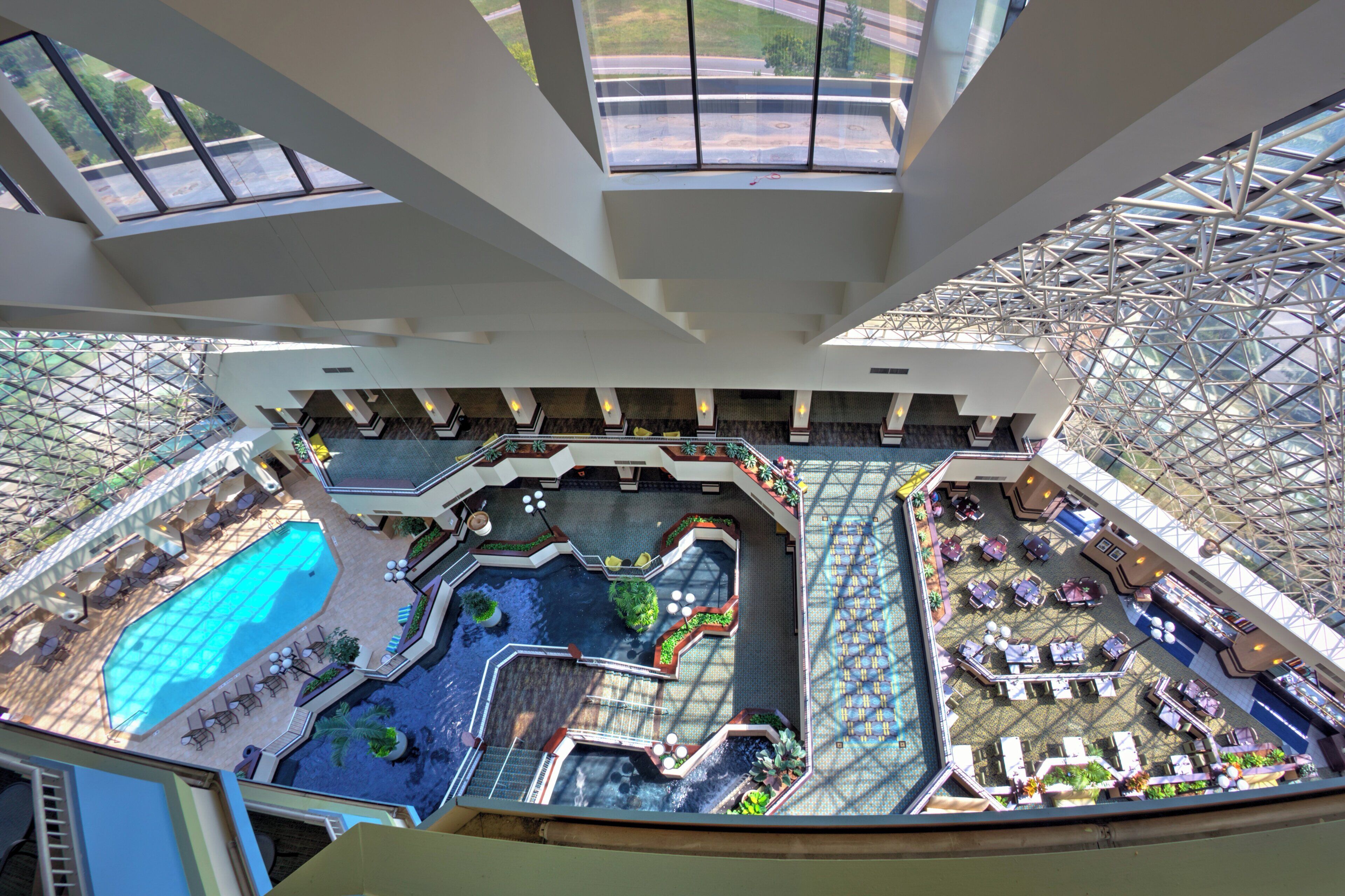 A high-ceiling atrium with a central water feature, seating areas, and a pool.