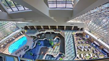 A high-ceiling atrium with a central water feature, seating areas, and a pool.