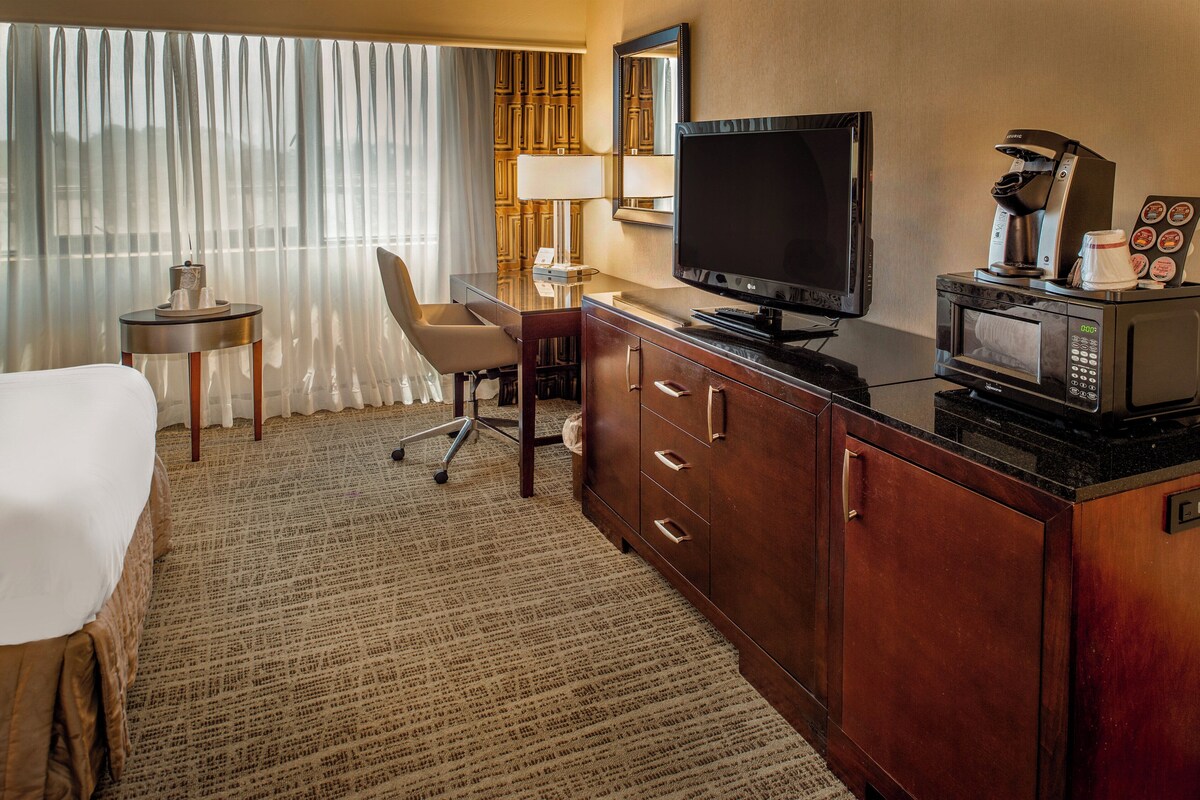 A hotel room with a bed, a desk with a chair, a television, a coffee maker, and a microwave.
