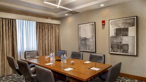 A conference room with a long table, six chairs, water bottles, and two abstract paintings on the walls.