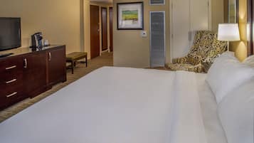 A hotel room with a large bed, a desk with a coffee maker, a chair, and a television.