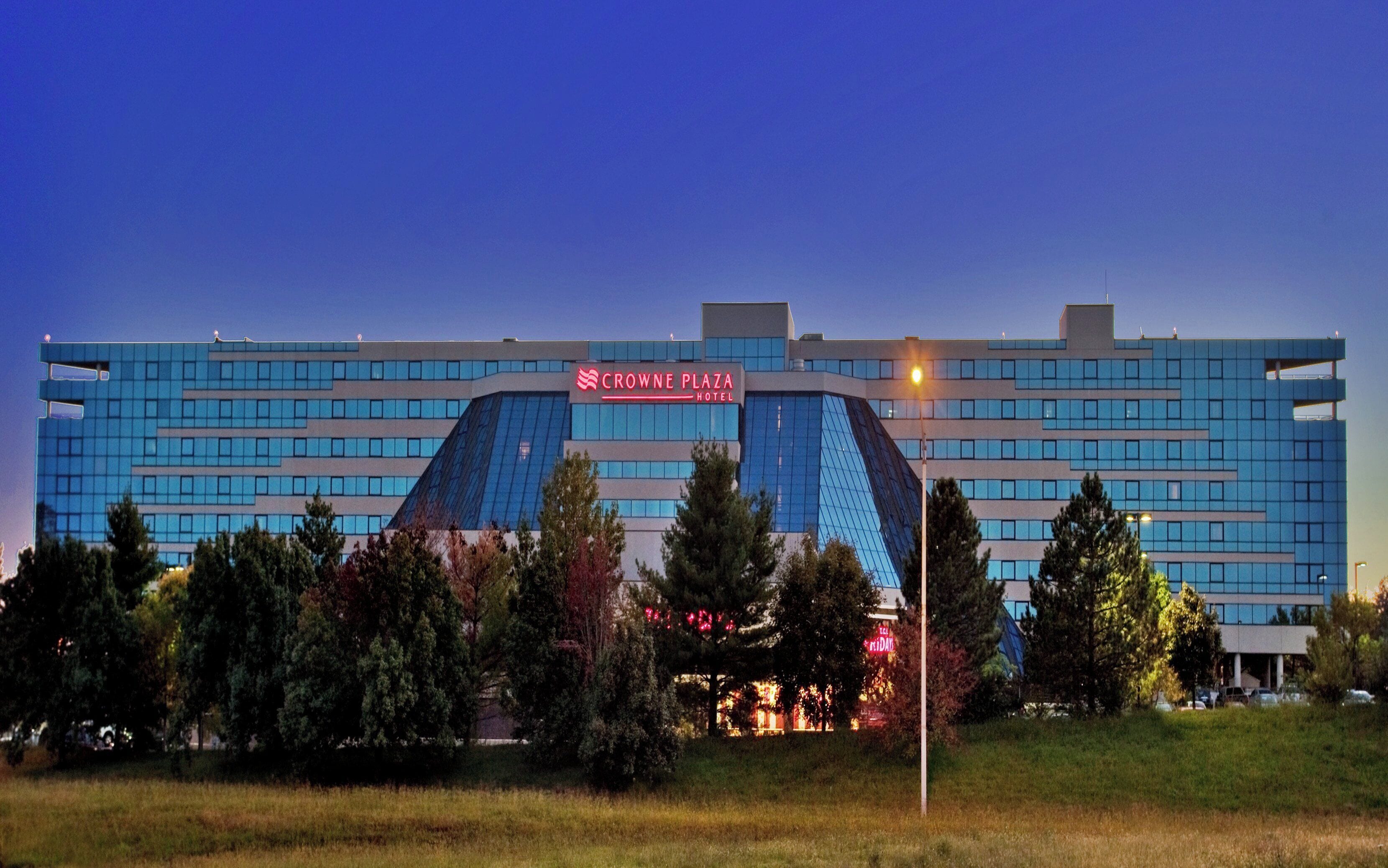 A modern hotel with a prominent sign, multiple floors, and a parking area in front.