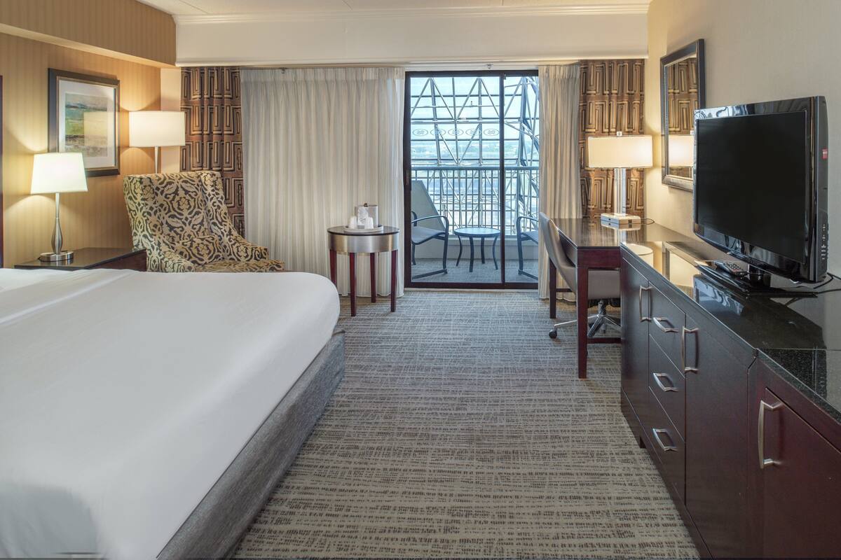 Une chambre d’hôtel avec un grand lit, un bureau avec une télévision, une chaise et une vue sur le balcon extérieur.