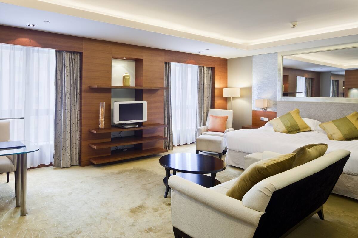 A hotel room with a bed, a sofa, a TV, a coffee table, and a desk with a chair.