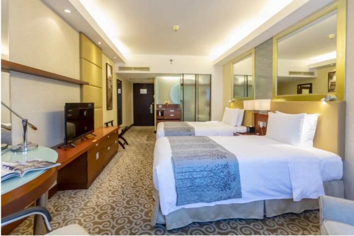 Habitación de hotel con dos camas, un escritorio con una silla, televisor y un espejo grande.