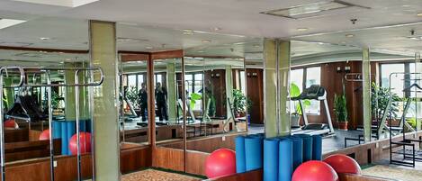A gym with exercise equipment, mirrors, and a patterned carpet.