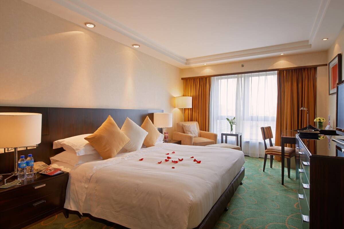 A hotel room with a large bed, a desk, a chair, and a window with curtains.