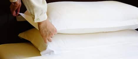 A hand adjusting a white pillow on a bed.
