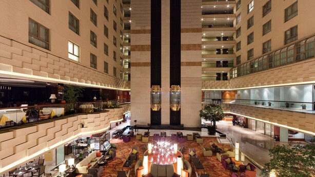 Un espacioso vestíbulo de hotel con una zona de estar central, varios pisos y un diseño moderno.