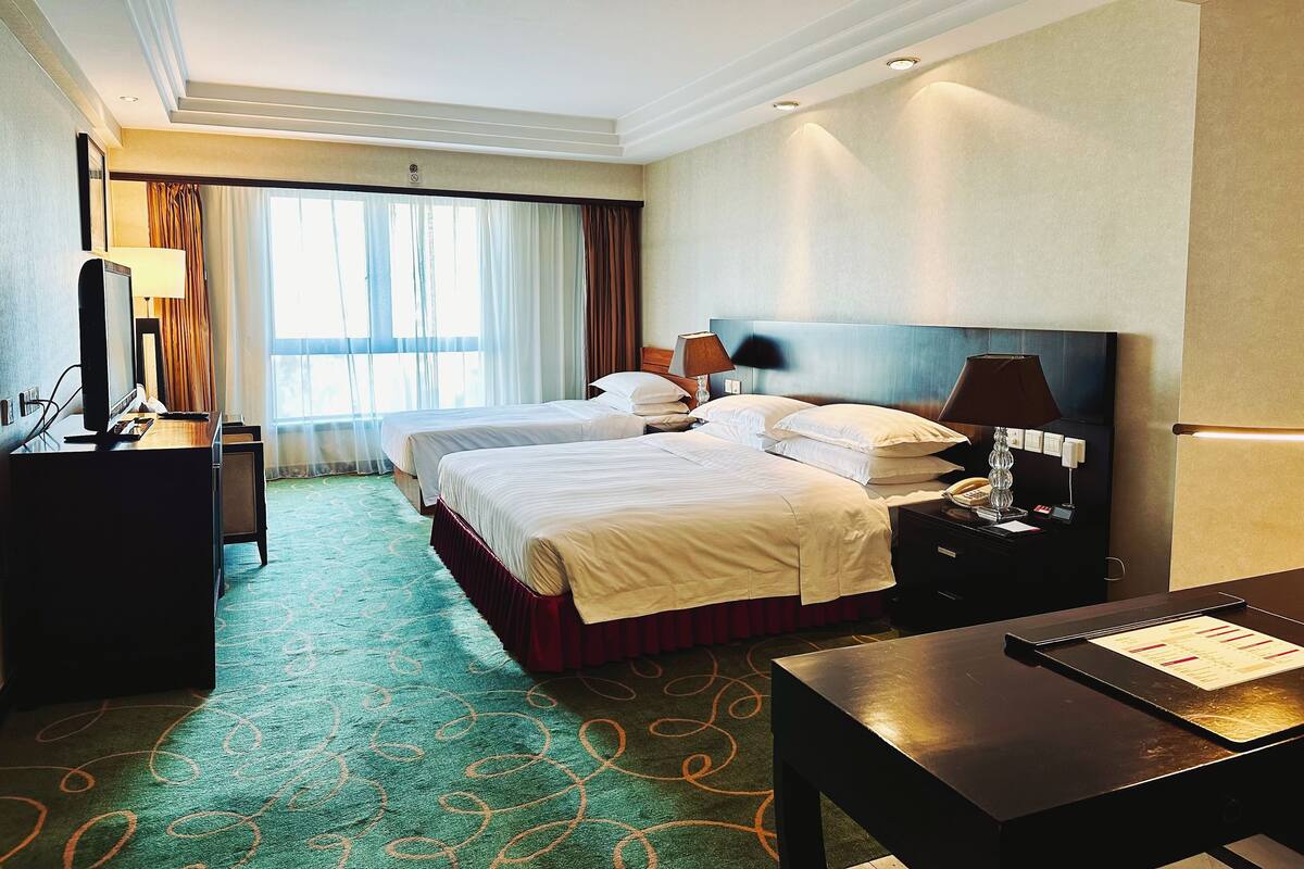 A hotel room with two beds, a desk, a chair, a TV, and a window with curtains.