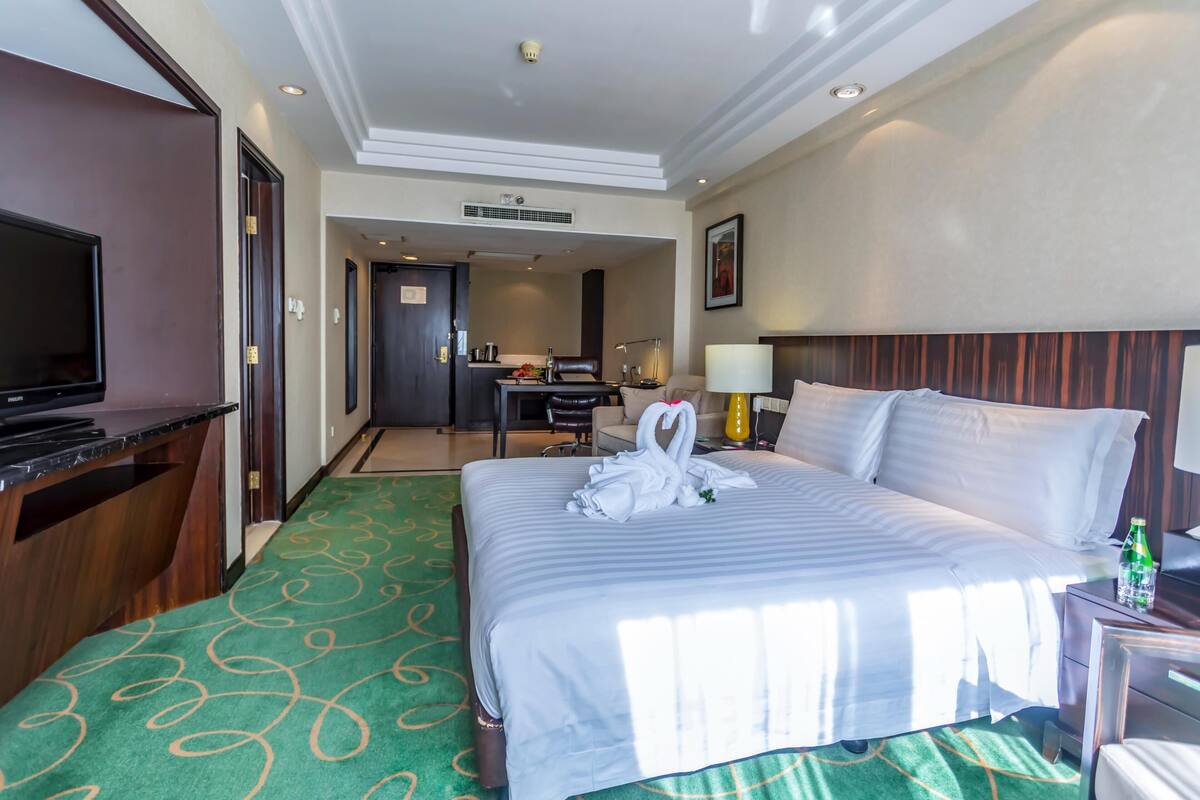 A hotel room with a bed, a desk, a television, and a bathroom visible in the background.