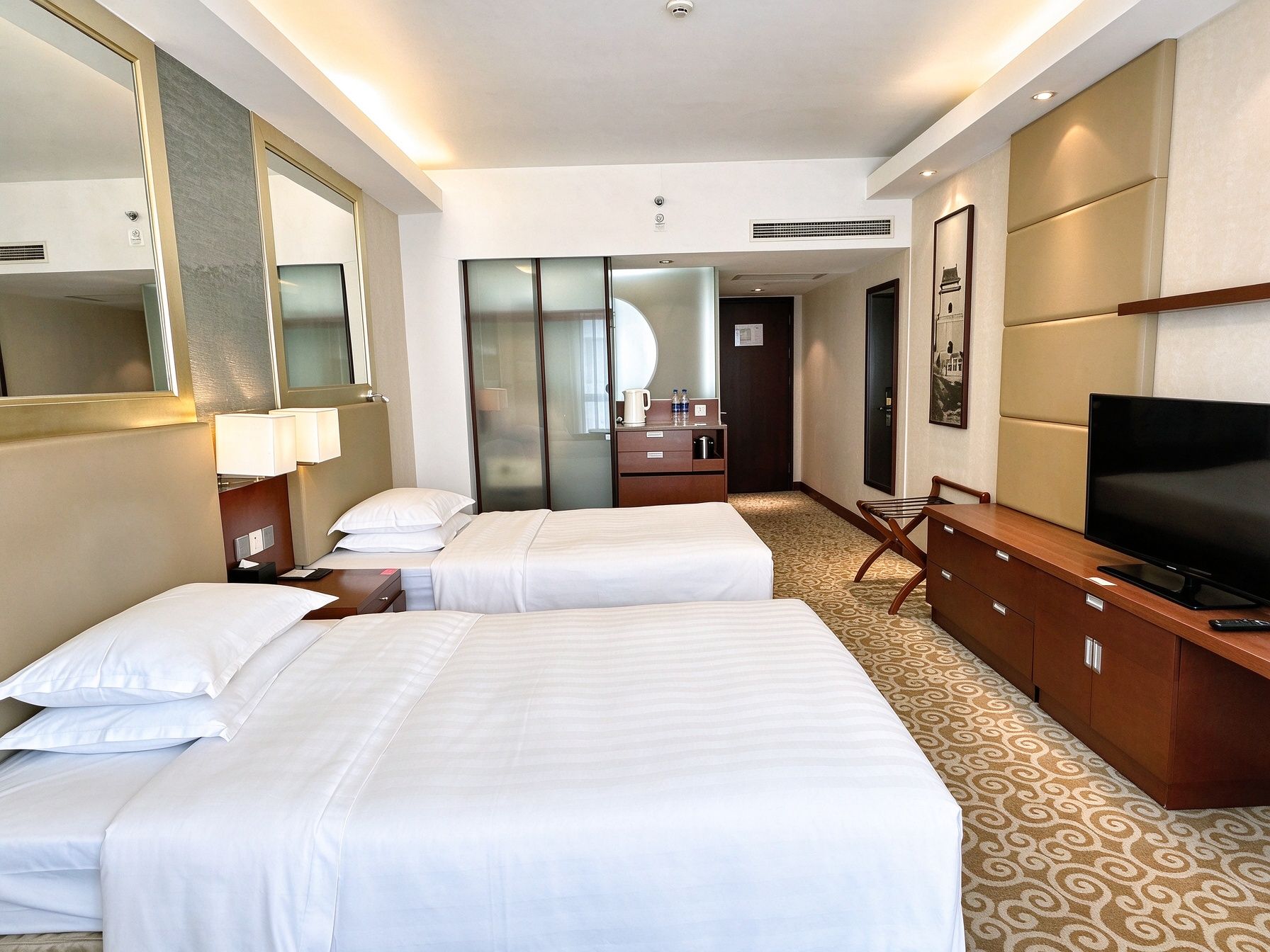 Quarto de hotel com duas camas, televisão, escrivaninha e espelho.