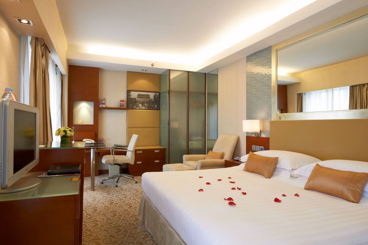 A hotel room with a large bed, a desk with a computer, a chair, a television, and a mirror.