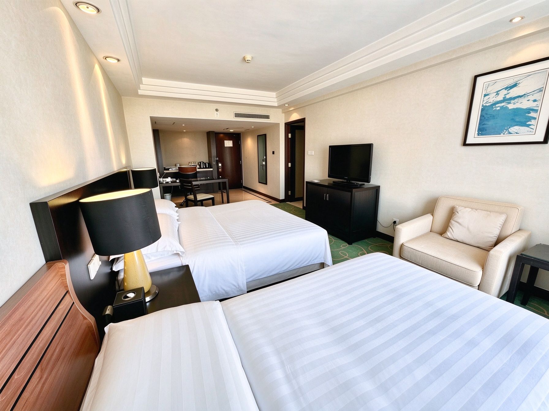 A hotel room with two beds, a desk, a chair, a television, and a framed picture on the wall.
