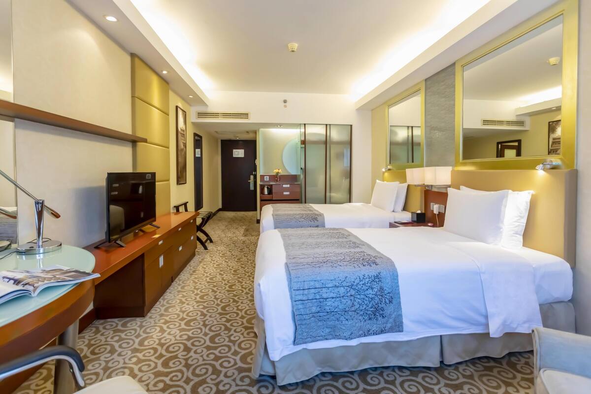 A hotel room with two beds, a desk with a computer, a TV, and a large mirror.