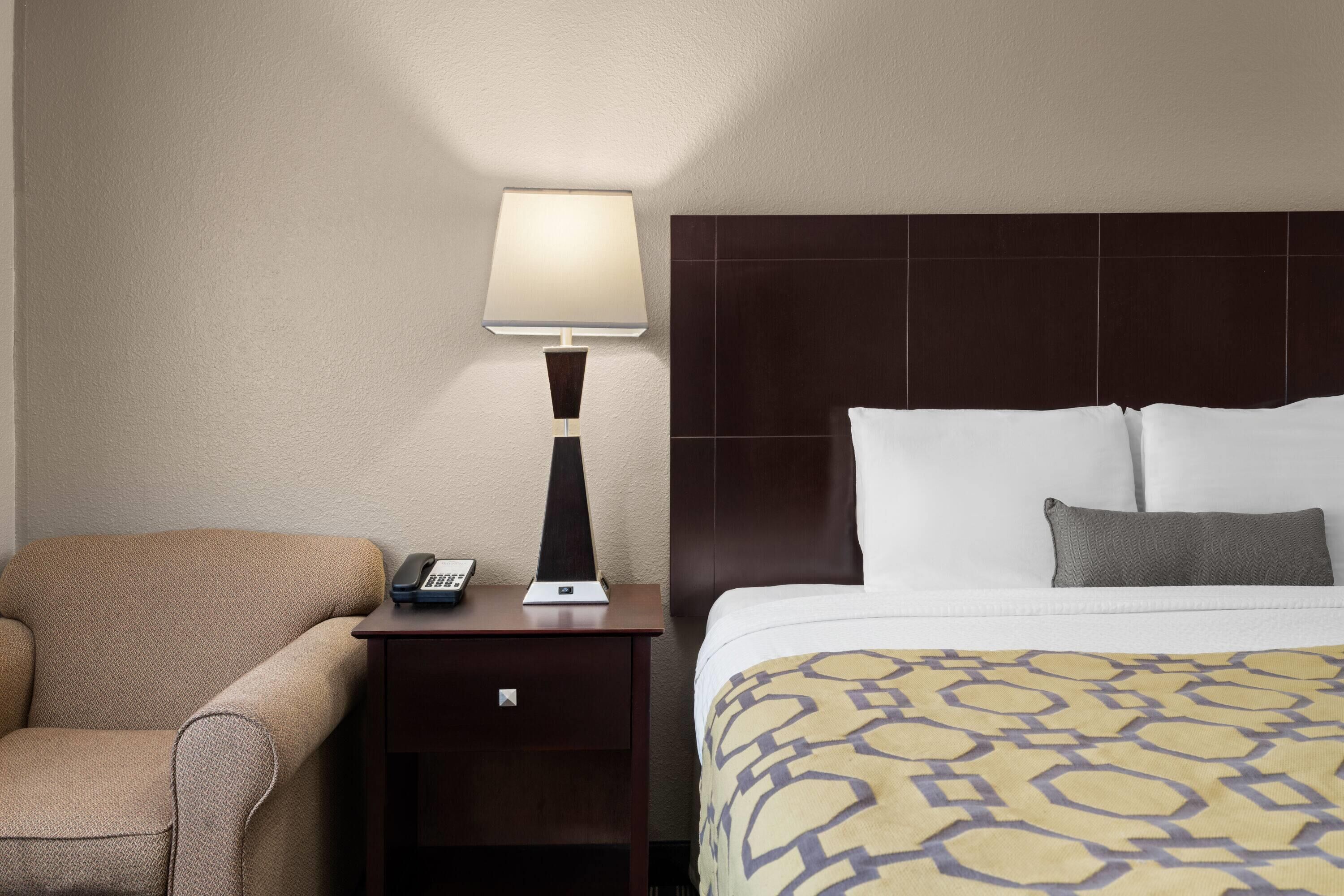 Una habitación de hotel con una cama, una mesita de noche con lámpara, un teléfono y una silla.