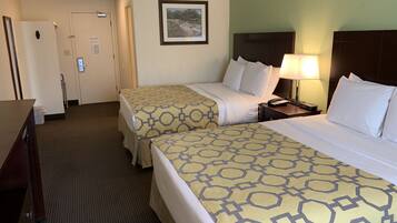 A hotel room with two beds, a desk, a chair, a door, and a framed picture on the wall.