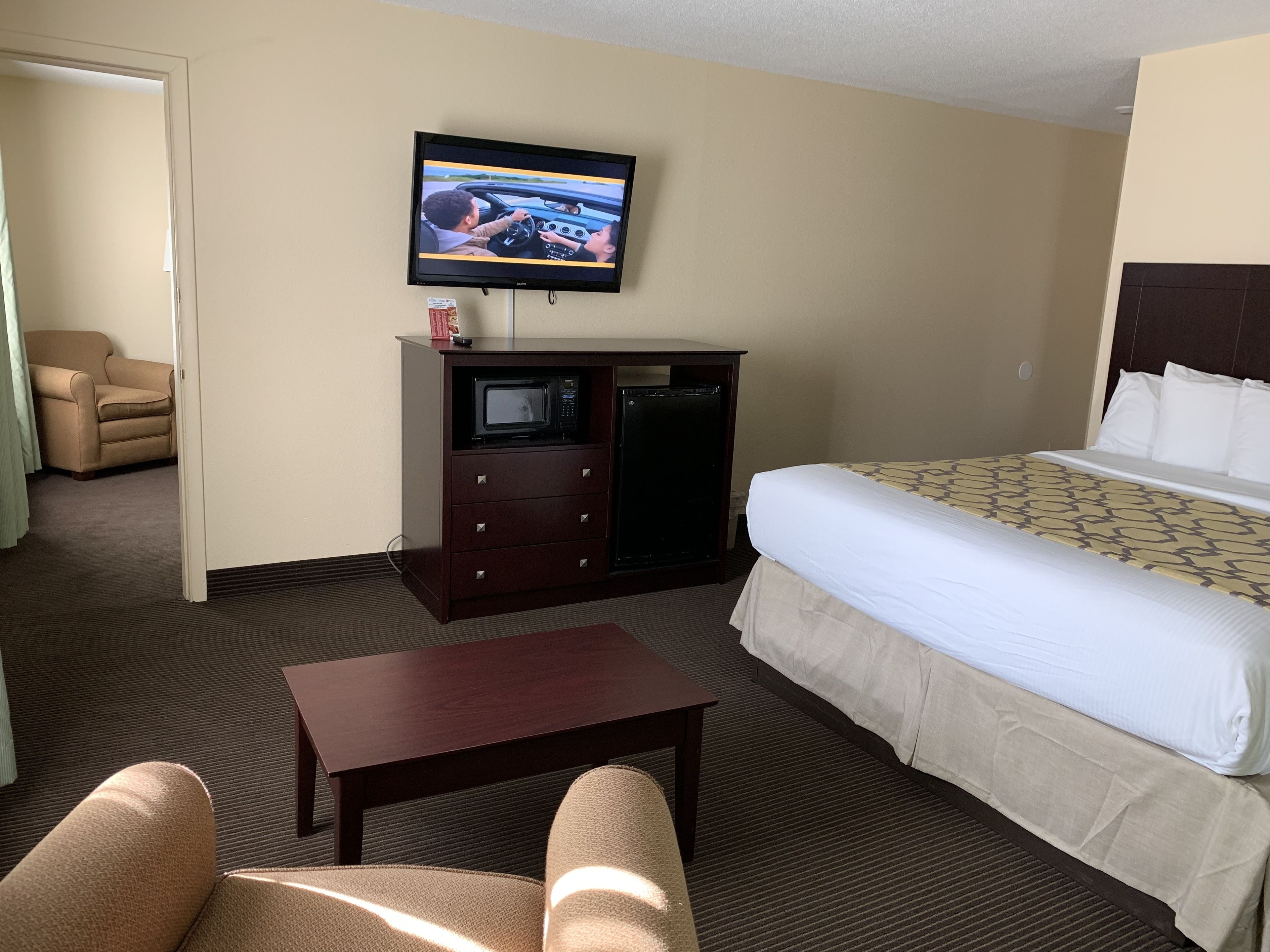 A hotel room with a bed, a television, a microwave, a small table, and a chair.